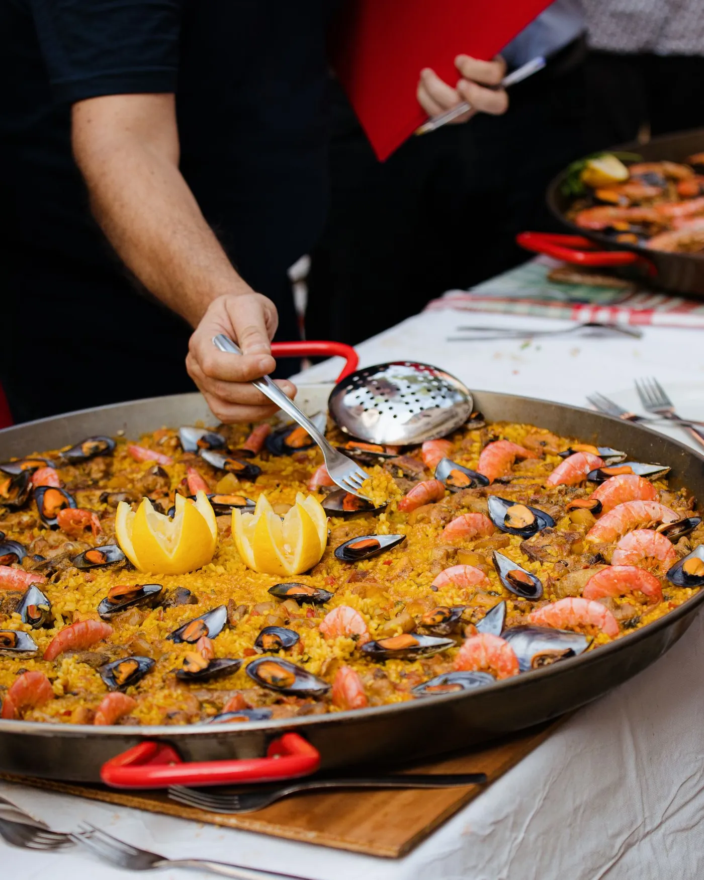 Paella de marisco recién hecha en una paellera grande, servida sobre una mesa con mantel blanco.