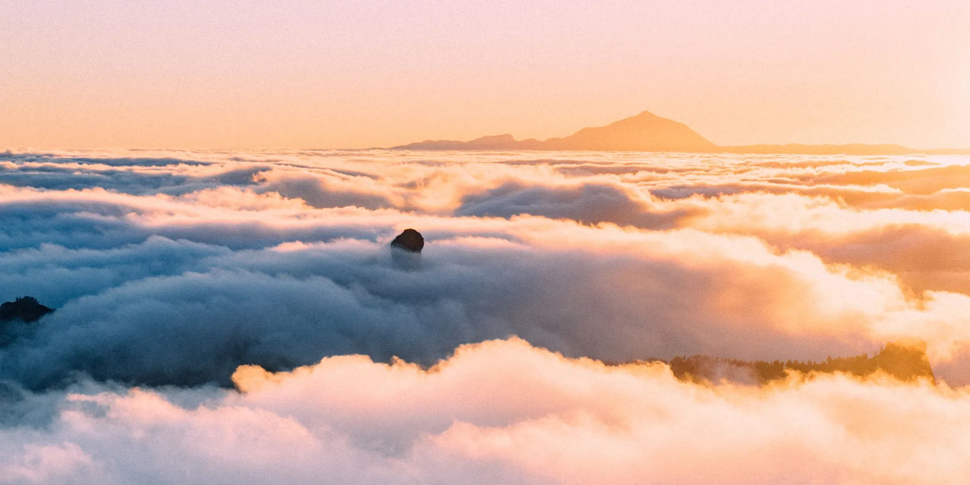 Amanecer sobre el mar de nubes desde la cumbre de Gran Canaria, con el Roque Nublo asomando y la silueta del Teide en el horizonte.