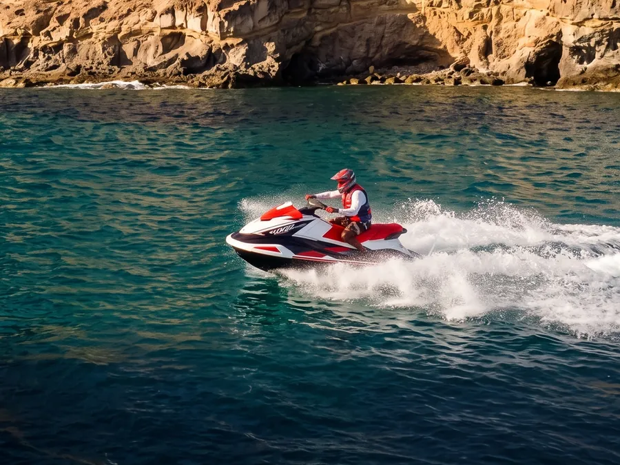 Una moto de agua cruza a toda velocidad el agua turquesa de una cala, al pie de un acantilado.
