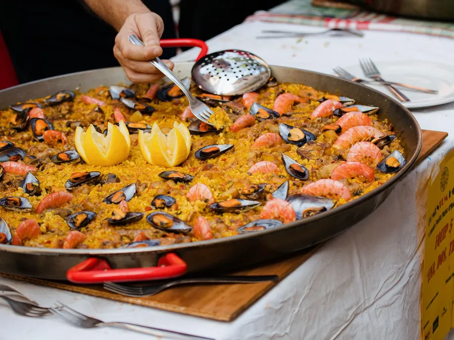 Paella de marisco recién hecha en la paellera, con mejillones, gambas y limón, servida sobre una mesa vestida de blanco.