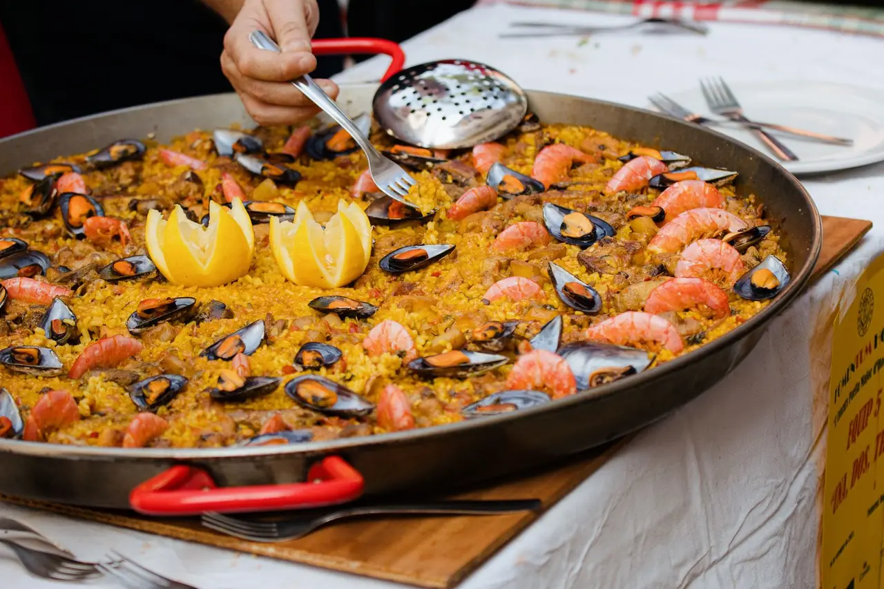 Paella de marisco recién hecha en la paellera, con mejillones, gambas y limón, servida sobre una mesa vestida de blanco.