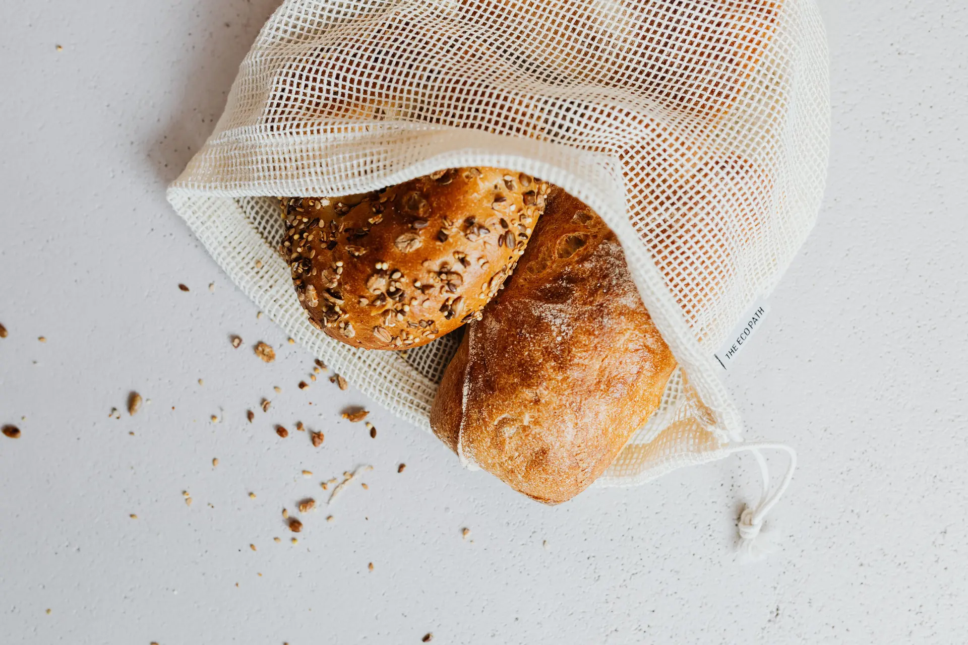 Dos panes recién horneados, uno de semillas y una chapata enharinada, dentro de una bolsa de malla de algodón.