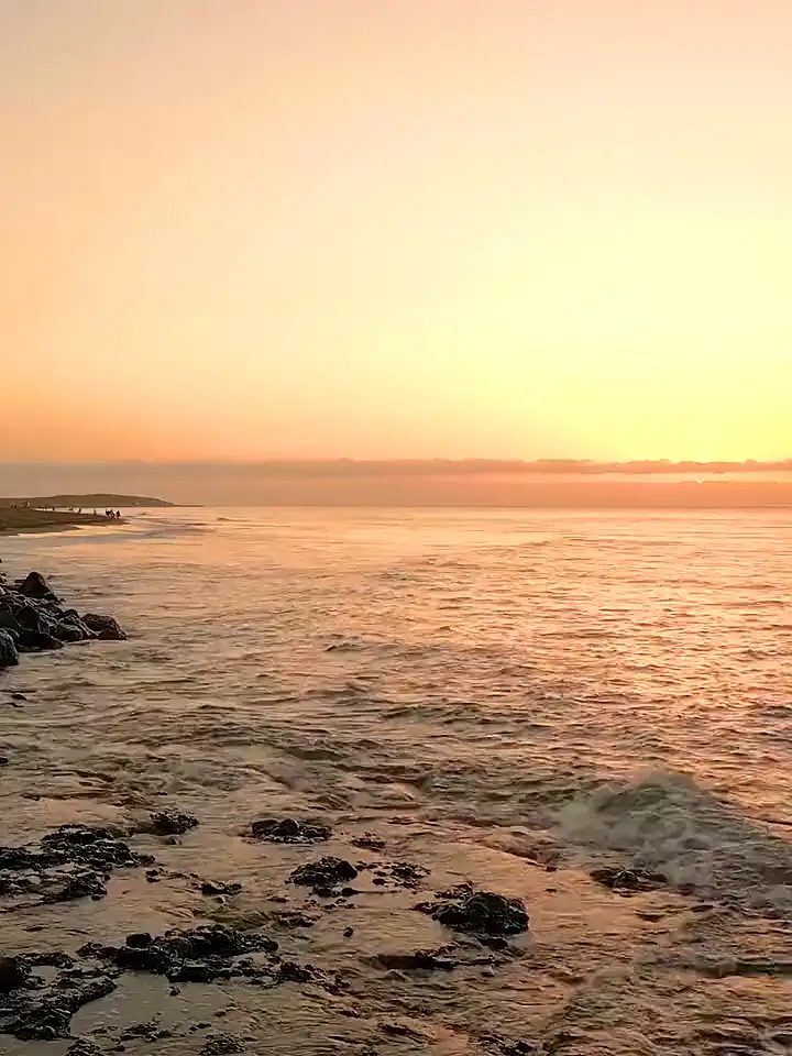 Atardecer sobre la costa sur de Gran Canaria, con la espuma rompiendo entre las rocas y el sol bajo en el horizonte.